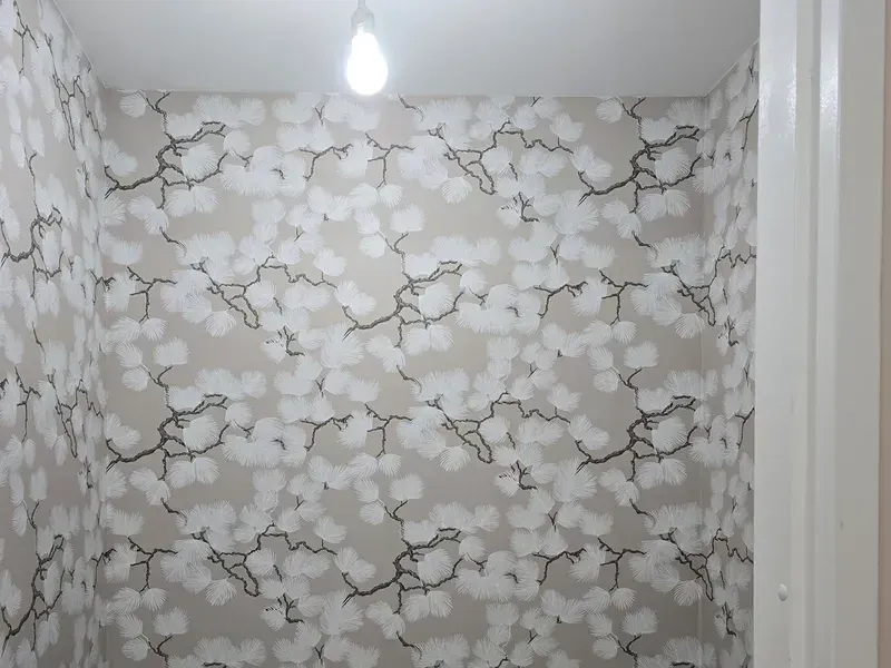 Toilet met vliesbehang in een patroon van zwarte takken en witte bloesem op een beige ondergrond, boven donkerblauwe tegels.