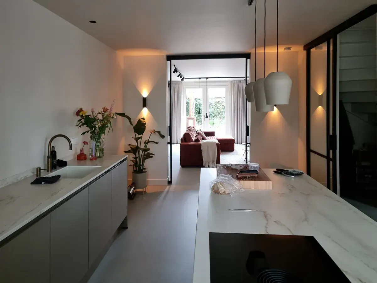 Lange keuken met woonkamer: strakke witte wanden, een marmeren werkblad en warme wandlampen.