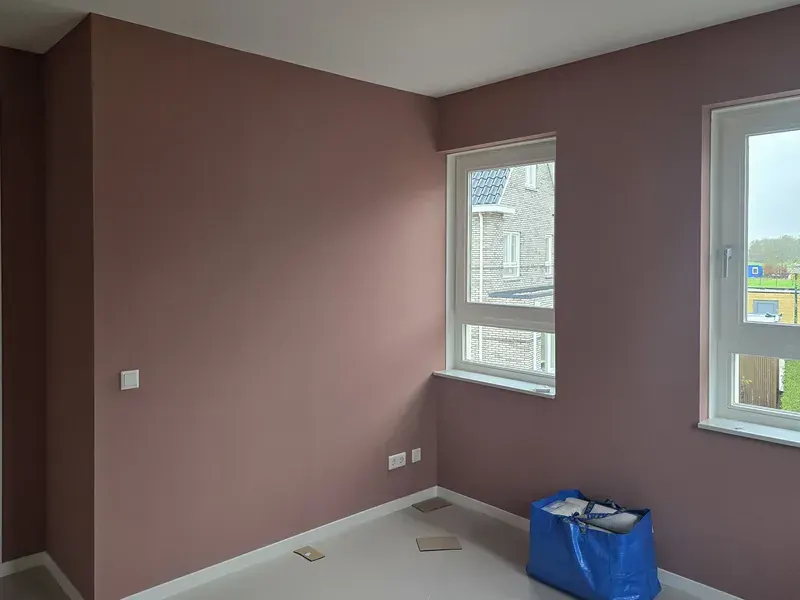 Lege kamer in een nieuwbouwwoning met oudroze geschilderde wanden, twee ramen en een lichte vloer.