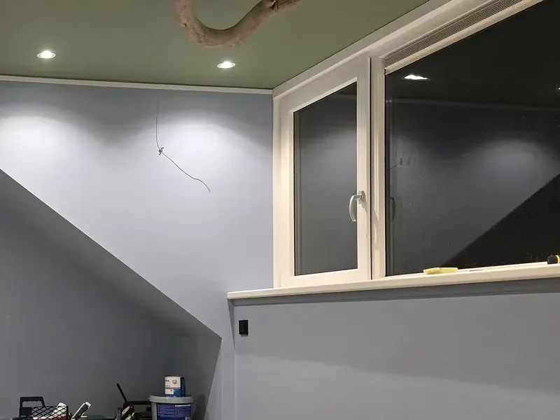 Zolderkamer met lichtblauw geschilderde wanden, een schuine wand en een raam in de dakkapel.